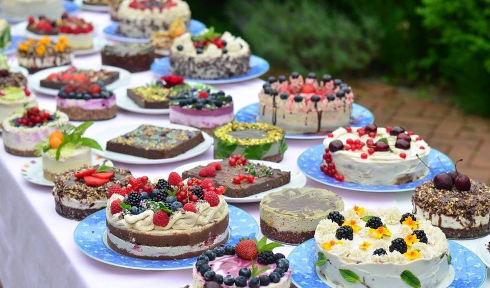 Auf dem Bild ist ein grosser Tisch zu sehen, welcher vollständig von unterschiedlich grossen, farbigen Torten und Kuchen aller Arten bedeckt ist.